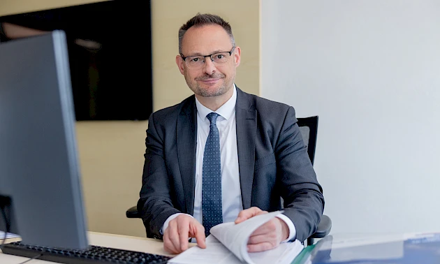Thomas Rickmann sitzt an einem Schreibtisch vor einem Computer. Er ist Experte für Generationenmanagement und Ruhestandsplanung bei der Volksbank Oberberg.“