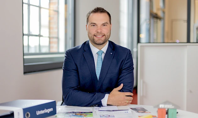 Gewerbekundenberater Frankjörn Schell sitzt an einem Schreibtisch und lächelt.