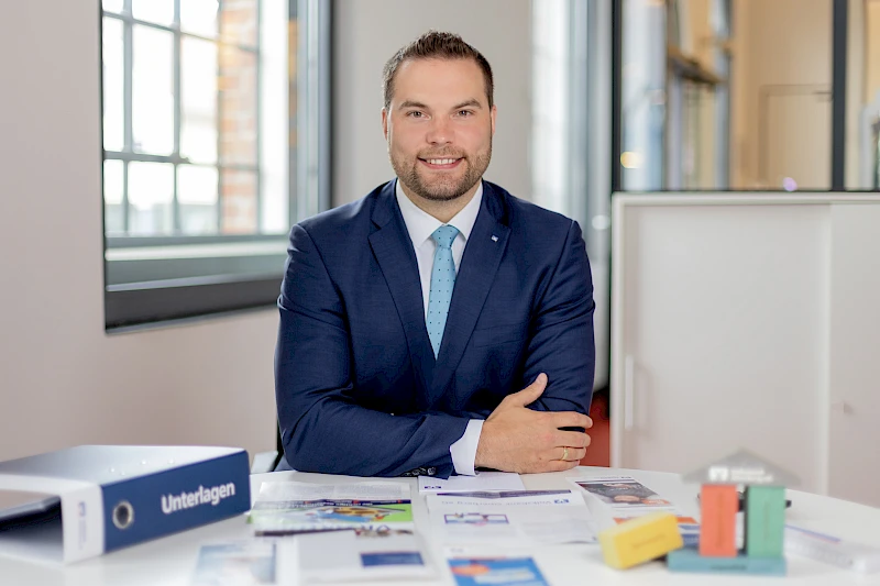 Gewerbekundenberater Frankjörn Schell sitzt an einem Schreibtisch und lächelt.