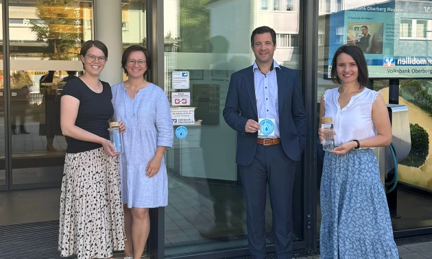 Drei Frauen und ein Mann lächeln vor der Eingangstür der Volksbank-Hauptgeschäftstelle in Wiehl.