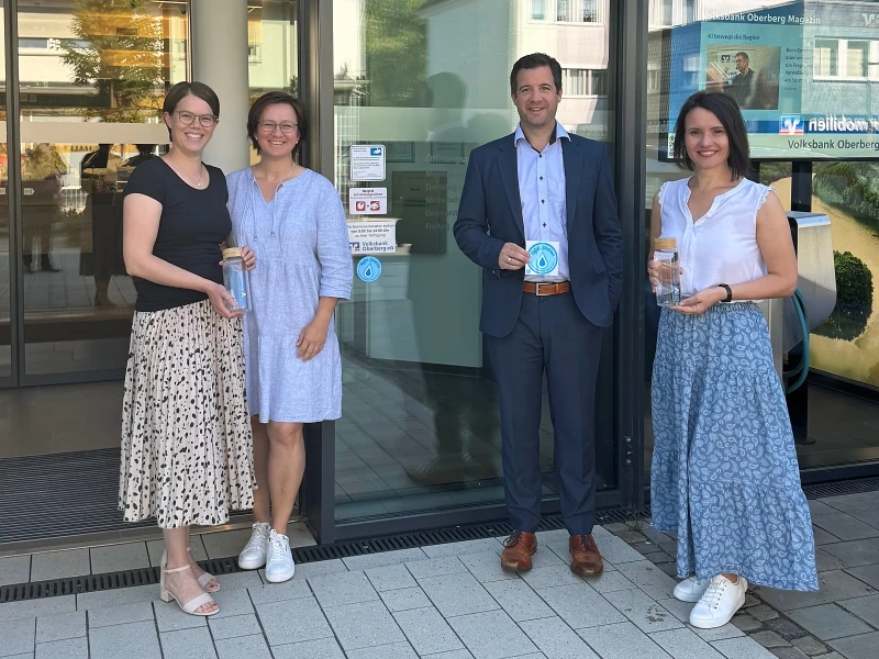 Drei Frauen und ein Mann lächeln vor der Eingangstür der Volksbank-Hauptgeschäftstelle in Wiehl.