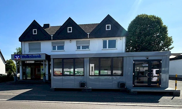 Außenansicht der Geschäftsstelle der Volksbank Oberberg in Drabenderhöhe mit davor aufgestellten Containern als provisorischer Beratungs- und Servicebereich während der Umbauphase.