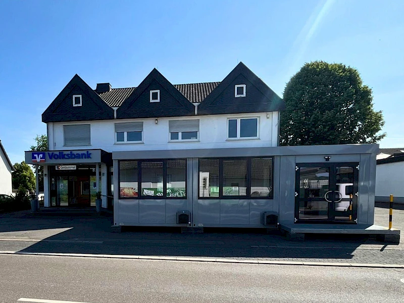 Außenansicht der Geschäftsstelle der Volksbank Oberberg in Drabenderhöhe mit davor aufgestellten Containern als provisorischer Beratungs- und Servicebereich während der Umbauphase.