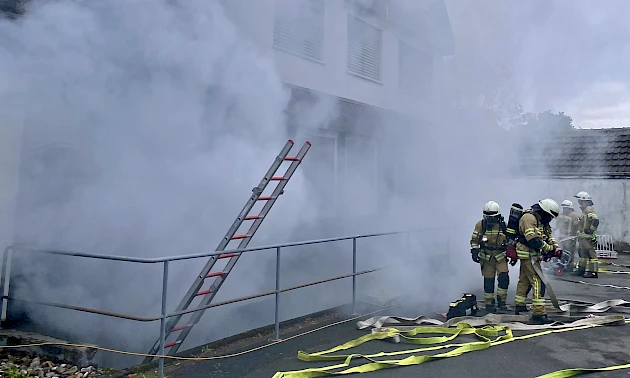 Vier Feuerwehrleute stehen vor der verrauchten Volksbank-Geschäftsstelle in Drabenderhöhe.