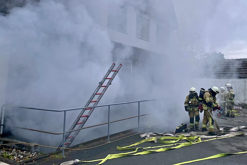 Vier Feuerwehrleute stehen vor der verrauchten Volksbank-Geschäftsstelle in Drabenderhöhe.