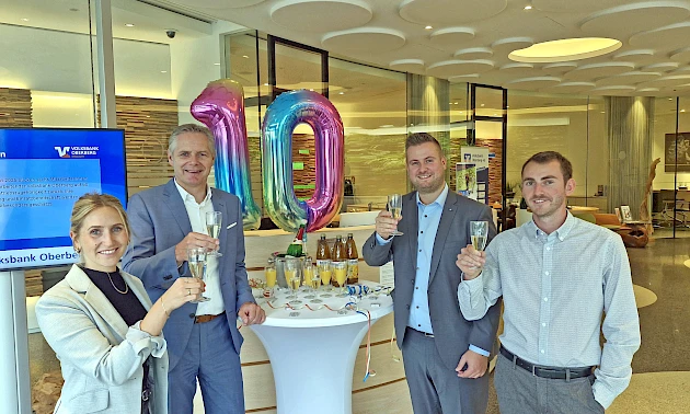 Vier Personen stoßen anlässlich des 10-jährigen Jubiläums der Geschäftsstelle Forum Gummersbach der Volksbank Oberberg an. Von links: Miriam Elsner, Niederlassungsleiter Henning Zöller, Geschäftsstellenleiter Justin Wagner und Mika Steeg. Sie lächeln und