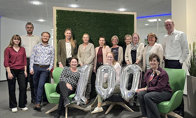 Das Team der Niederlassung Radevormwald lächelt und hält eine 100 aus Luftballons in die Höhe.