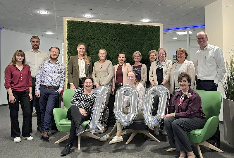 Das Team der Niederlassung Radevormwald lächelt und hält eine 100 aus Luftballons in die Höhe.