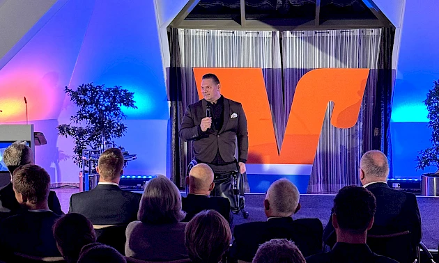Florian Sitzmann auf der Bühne im Forum der Volksbank Oberberg in Wiehl während seines Vortrags beim UnternehmerForum. Im Vordergrund sind Köpfe des Publikums zu sehen.