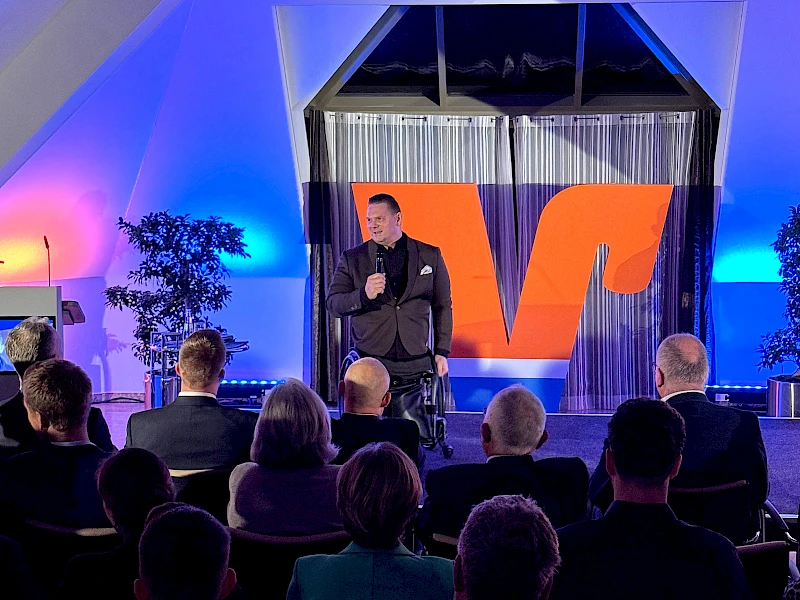 Florian Sitzmann auf der Bühne im Forum der Volksbank Oberberg in Wiehl während seines Vortrags beim UnternehmerForum. Im Vordergrund sind Köpfe des Publikums zu sehen.