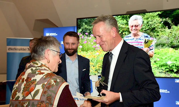 Gunhild Hartmann, die Siegerin des Sommerwettbewerbs, nimmt lächelnd den Siegerpokal von Ingo Stockhausen, dem Vorstandsvorsitzenden der Volksbank Oberberg, entgegen