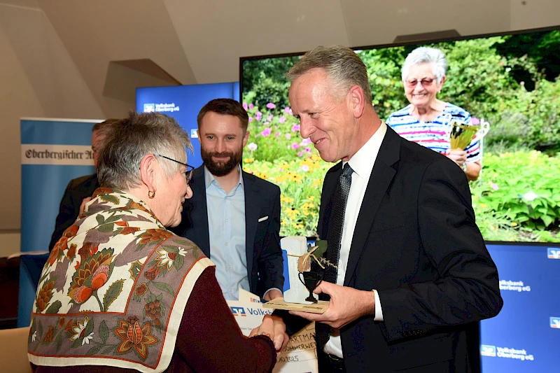Gunhild Hartmann, die Siegerin des Sommerwettbewerbs, nimmt lächelnd den Siegerpokal von Ingo Stockhausen, dem Vorstandsvorsitzenden der Volksbank Oberberg, entgegen