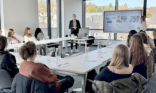Vortragssituation in der Volksbank Oberberg Akademie: In einem großen Konferenzraum sitzen Schülerinnen und Schüler in U-Form an Tischen, während Sarina Scherbaum und Annabell Strauch vorne stehen und den Jugendlichen das Ausbildungsangebot der Volksbank
