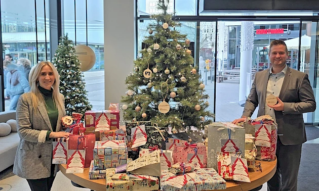 Miriam Elsner und Forum-Geschäftsstellenleiter Justin Wagner stehen im Forum Gummersbach neben einem geschmückten Weihnachtswunschbaum mit vielen verpackten Geschenken aus der Wunschbaumaktion der Volksbank Oberberg.