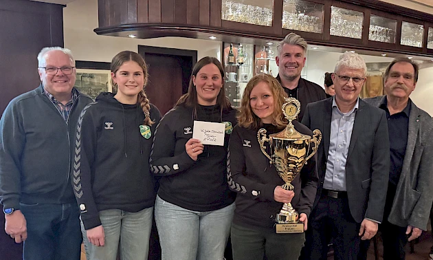 Gruppenfoto bei der Pokalübergabe: Niederlassungsleiter Michael Eiteneuer überreicht den Volksbank-Oberberg-Pokal an Spielerinnen der HC Gelpe/Strombach, die den Pokal in den Händen halten. Mehrere Beteiligte stehen gemeinsam in einem Innenraum.