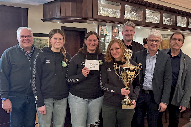 Gruppenfoto bei der Pokalübergabe: Niederlassungsleiter Michael Eiteneuer überreicht den Volksbank-Oberberg-Pokal an Spielerinnen der HC Gelpe/Strombach, die den Pokal in den Händen halten. Mehrere Beteiligte stehen gemeinsam in einem Innenraum.