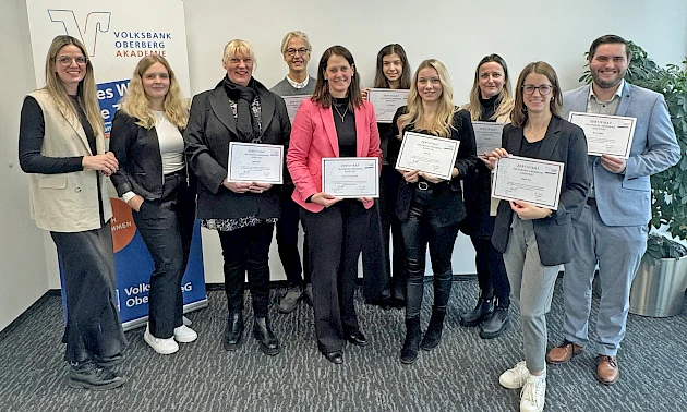 Gruppenfoto der erfolgreichen Absolventinnen und des Absolventen der Aufbauqualifizierung „Volksbank Oberberg Assistent“ mit ihren Zertifikaten, gemeinsam mit den Trainerinnen Lisa Dross und Mara Mischke in den Räumen der Volksbank Oberberg Akademie.