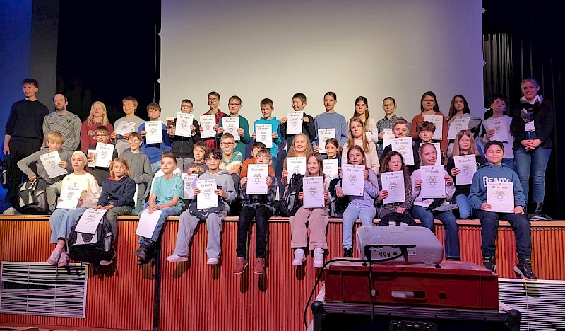 Gruppenfoto der ausgezeichneten Teilnehmerinnen und Teilnehmer der 65. Mathematik-Olympiade auf der Bühne des Hollenberg-Gymnasiums Waldbröl mit ihren Urkunden.