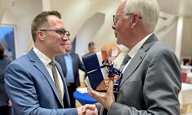 Dr. Udo Meyer überreicht Andreas Neumann bei einer Feierstunde in der Hauptstelle ein Geschenk und gratuliert ihm per Handschlag zum 40. Geburtstag.