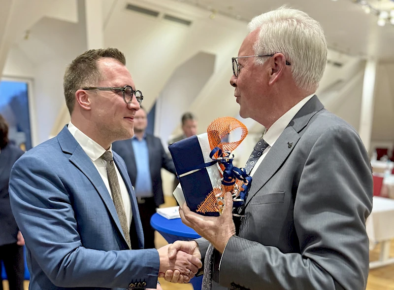 Dr. Udo Meyer überreicht Andreas Neumann bei einer Feierstunde in der Hauptstelle ein Geschenk und gratuliert ihm per Handschlag zum 40. Geburtstag.
