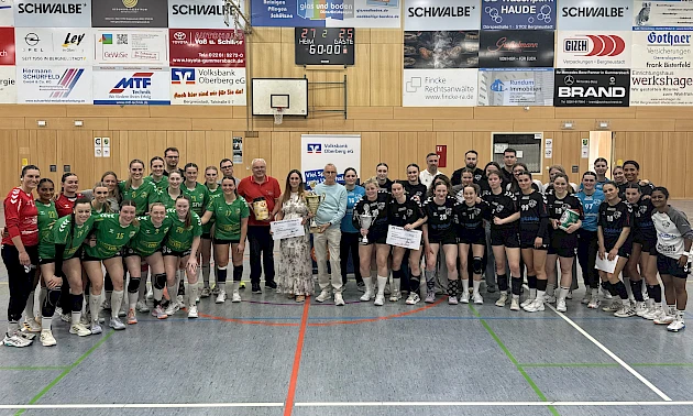 In einer Sporthalle stehen zwei Handballmannschaften mit Funktionären auf dem Spielfeld während einer Siegerehrung.