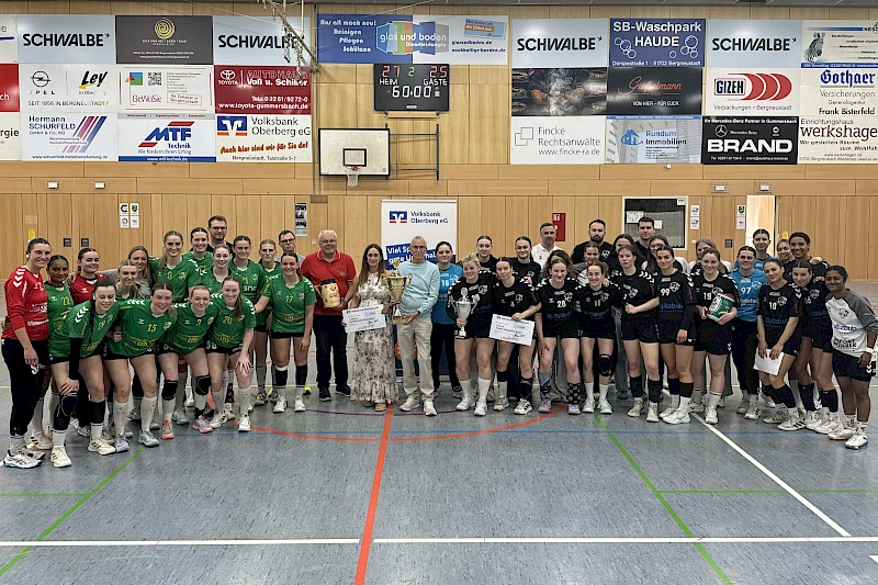 In einer Sporthalle stehen zwei Handballmannschaften mit Funktionären auf dem Spielfeld während einer Siegerehrung.