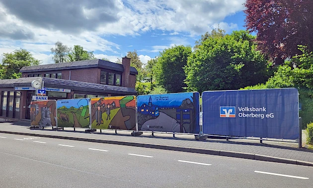 Großformatige Graffiti-Planen mit regionalen Motiven und Werten hängen an den Bauzäunen vor der Geschäftsstelle der Volksbank Oberberg in Bergneustadt, die aktuell modernisiert wird.