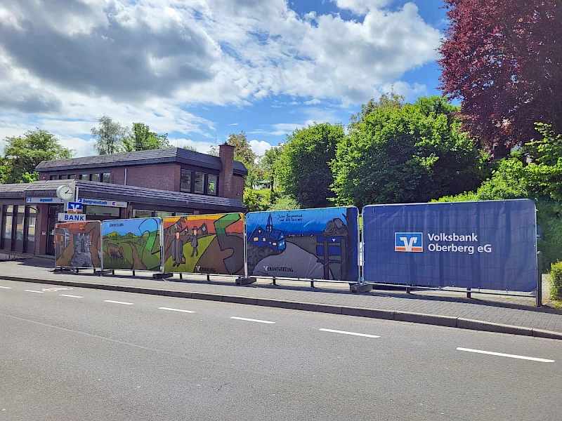 Großformatige Graffiti-Planen mit regionalen Motiven und Werten hängen an den Bauzäunen vor der Geschäftsstelle der Volksbank Oberberg in Bergneustadt, die aktuell modernisiert wird.