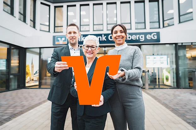 Drei Mitglieder der Volksbank Oberberg stehen vor dem Bankgebäude und symbolisieren die genossenschaftliche Mitgliedschaft und die Verbundenheit mit der Bank.