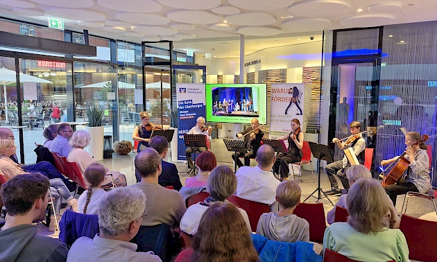 Konzertveranstaltung im Forum der Volksbank Oberberg: Mehrere Ensemblemitglieder spielen Geigen und Cello vor einem aufmerksam zuhörenden Publikum.