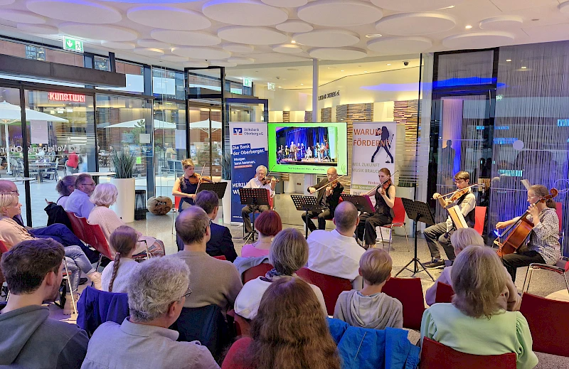 Konzertveranstaltung im Forum der Volksbank Oberberg: Mehrere Ensemblemitglieder spielen Geigen und Cello vor einem aufmerksam zuh&ouml;renden Publikum.