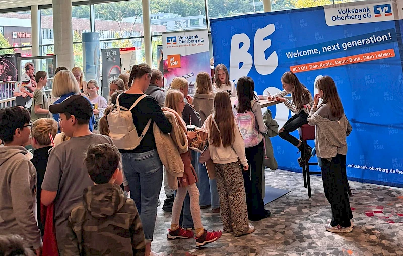 Bela und Charlotte Plass sitzen an einem Tisch im SEVEN Kinocenter Gummersbach und geben Autogramme. Vor ihnen wartet eine Schlange junger Kinog&auml;ste.