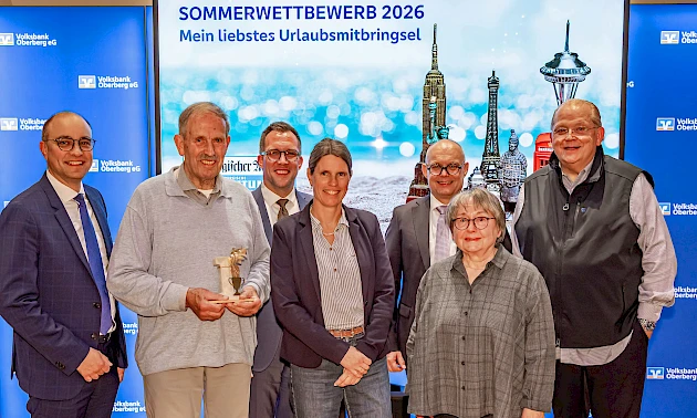 Die drei Erstplatzierten des Sommerwettbewerbs 2026 posieren bei der Preisverleihung gemeinsam mit Vertretern der Volksbank Oberberg und der Oberbergischen Volkszeitung vor der Wettbewerbswand.