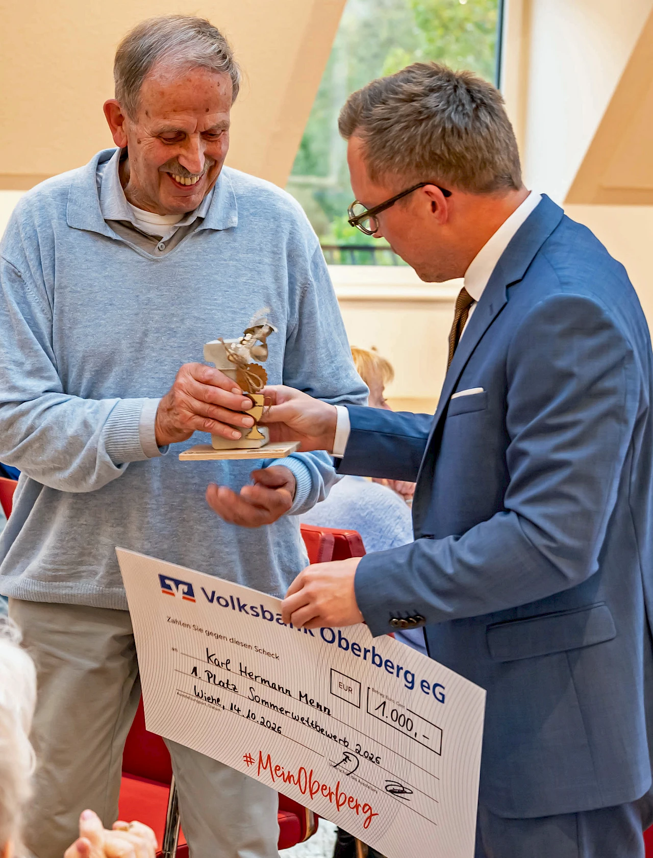 Scheckübergabe beim Sommerwettbewerb 2026. Karl Hermann Menn erhält von Andreas Neumann einen Siegerpokal und einen symbolischen Scheck über 1.000 Euro.