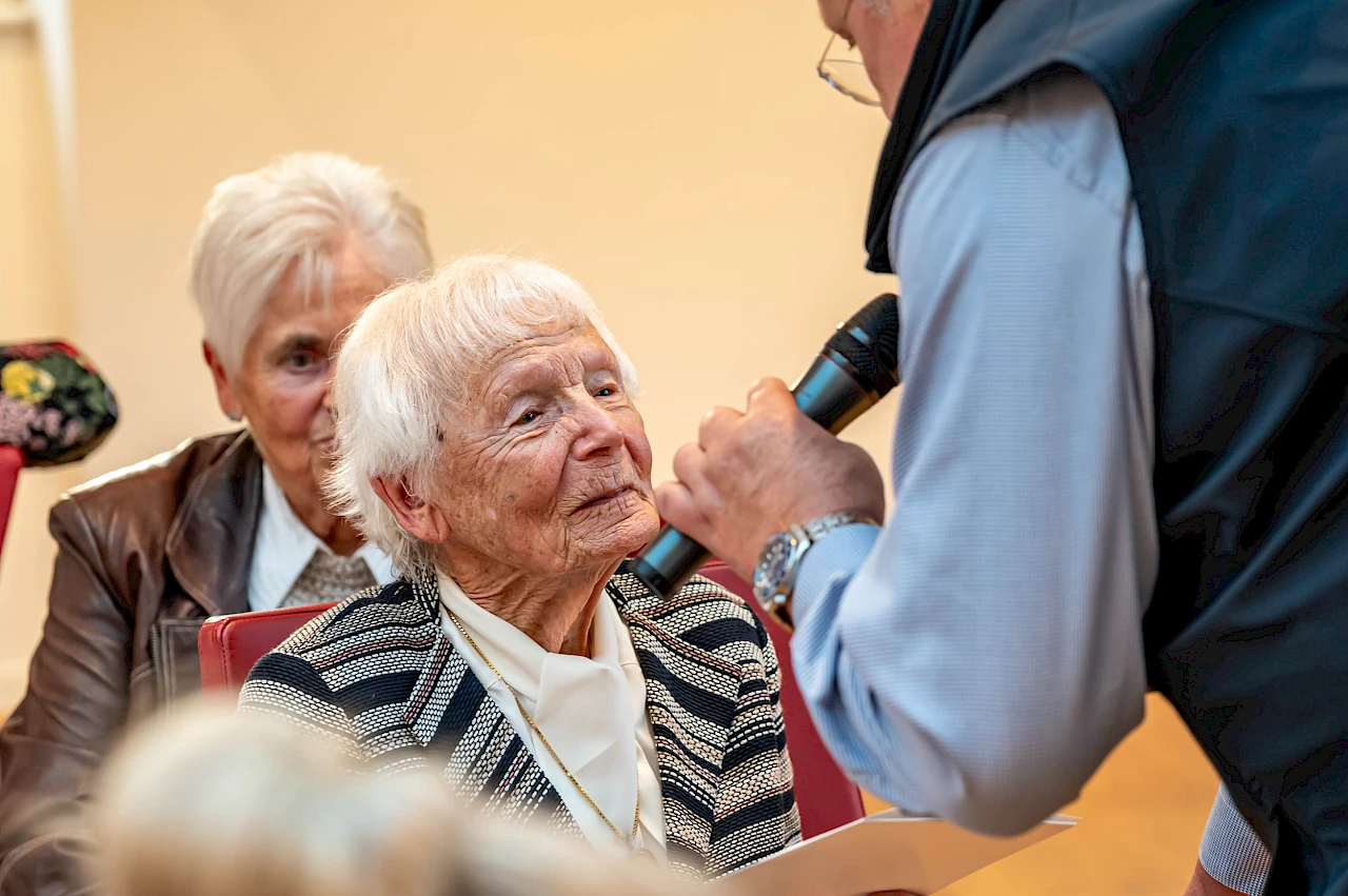 Waltraud Fischbach sitzt beim Ehrungsabend des Sommerwettbewerbs 2026 im Publikum und berichtet im Gespräch mit einem Moderator von ihrem Urlaubsmitbringsel aus Alaska und der damit verbundenen Reiseerinnerung.